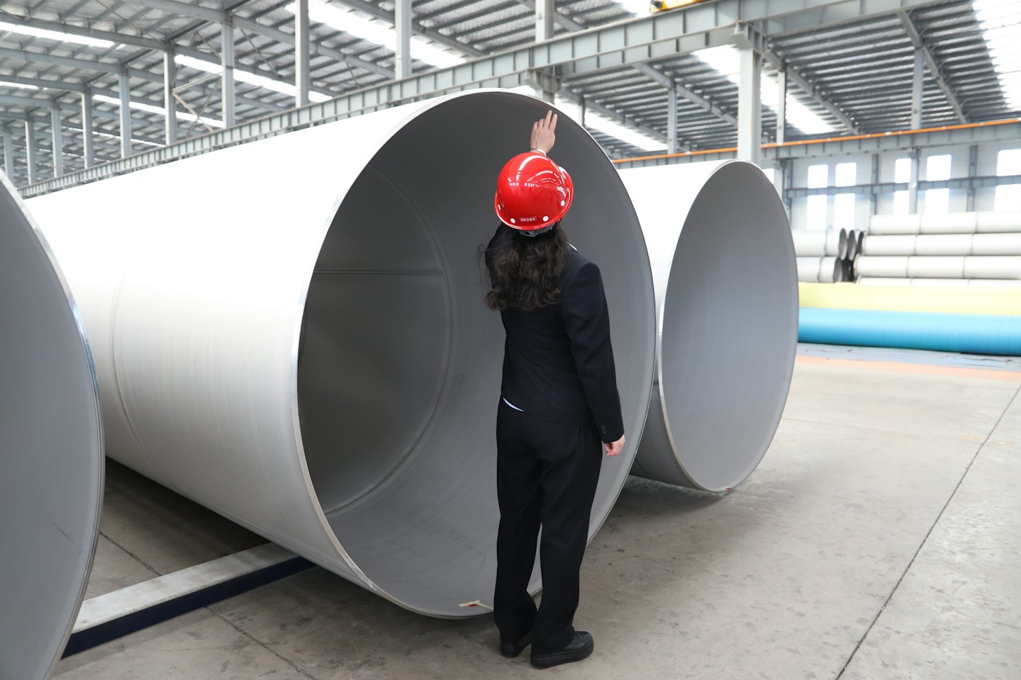 Home Engineer in a red hard hat points toward factory pipes.