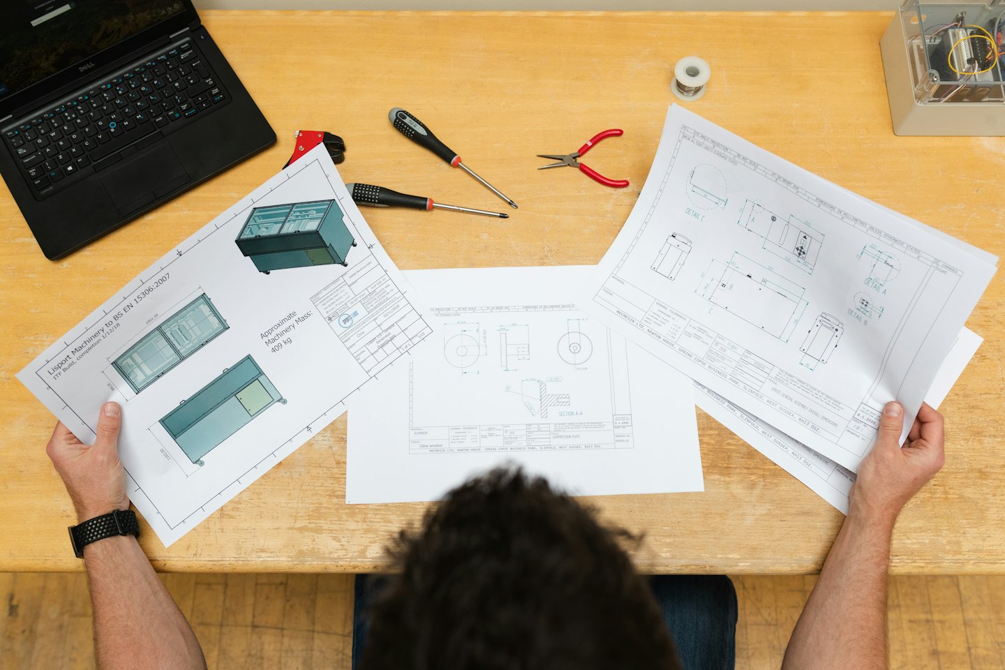 Booking Person reviewing blueprints with tools and laptop on desk.
